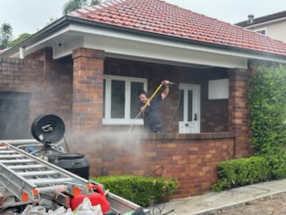 Worker using a pressure-washer lance on a red-brick house verandah